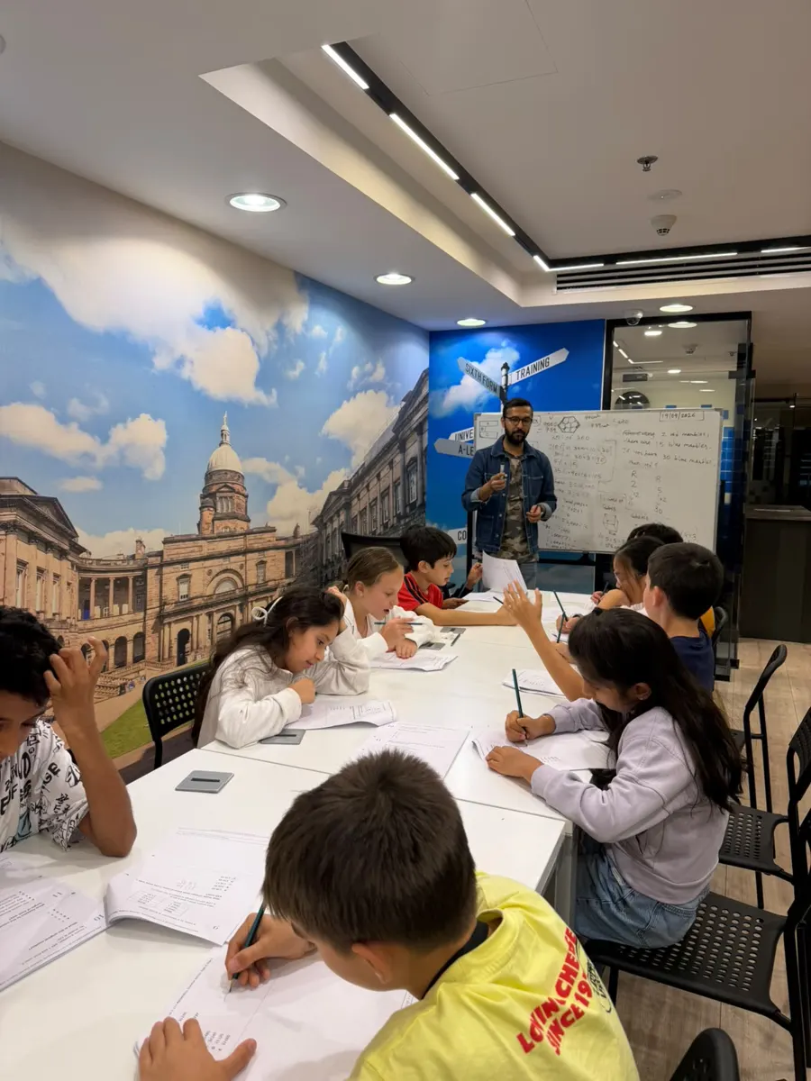 A teacher at the whiteboard with a small group of students working at a shared table at Improve ME Institute.